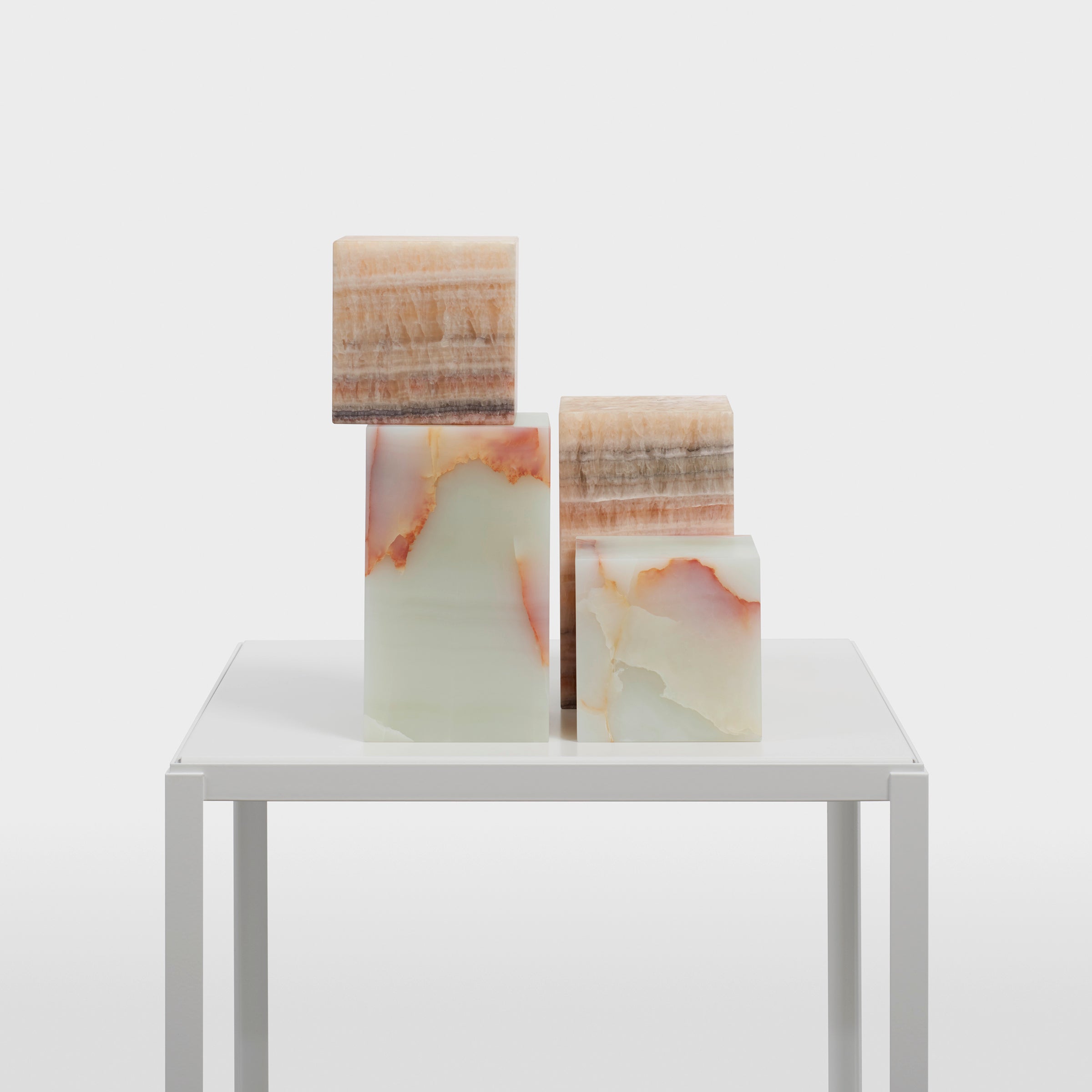 Four translucent AC11 STOP ONYX sculptures from the e15 collection, showcasing earthy tones and natural veining in beige, orange, and brown, are arranged on a modern white table against a plain background.