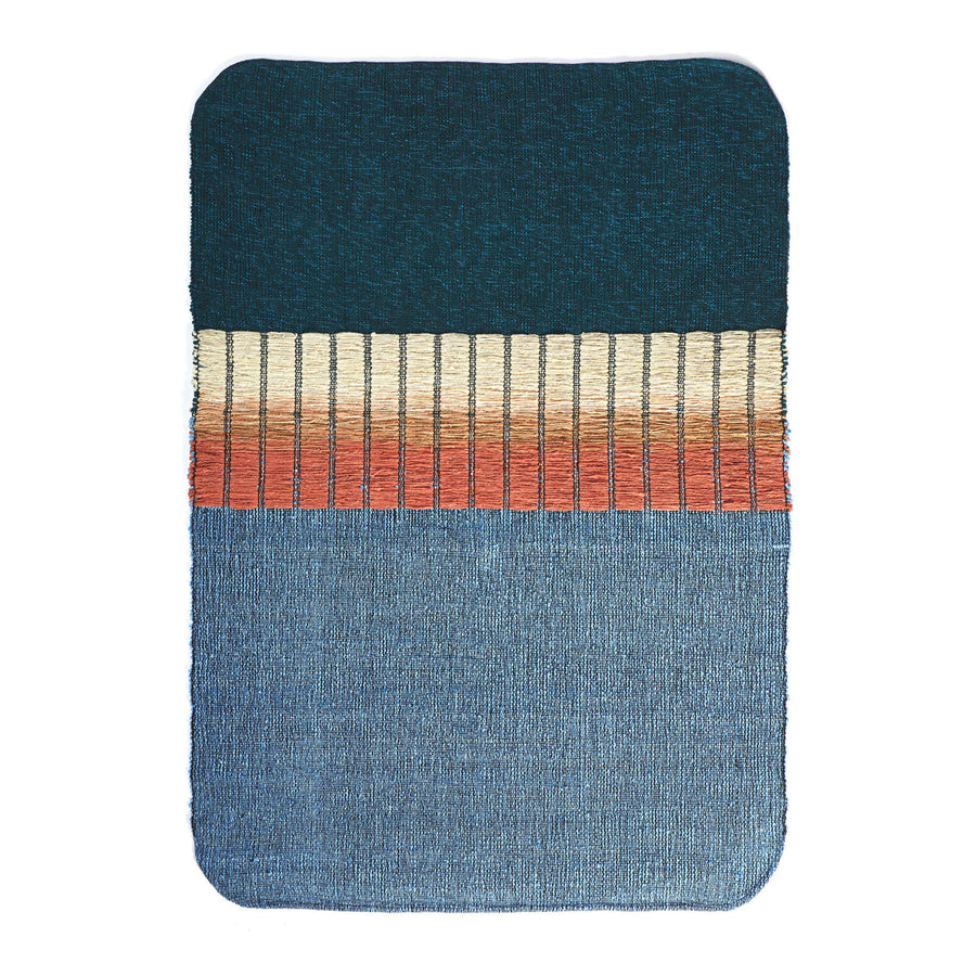 The Ames Balcones Rug is a hand-woven textile art piece with an elegant gradient: dark teal at the top, beige and orange stripes in the center, and light blue at the bottom. The edges are beautifully rounded.
