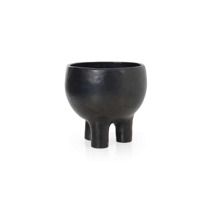 The Barro Pot 2 by Ames features a black matte finish and sculptural three-legged design. Sitting against a white background, its wide rounded body showcases Colombian potterys artistry and modern simplicity.