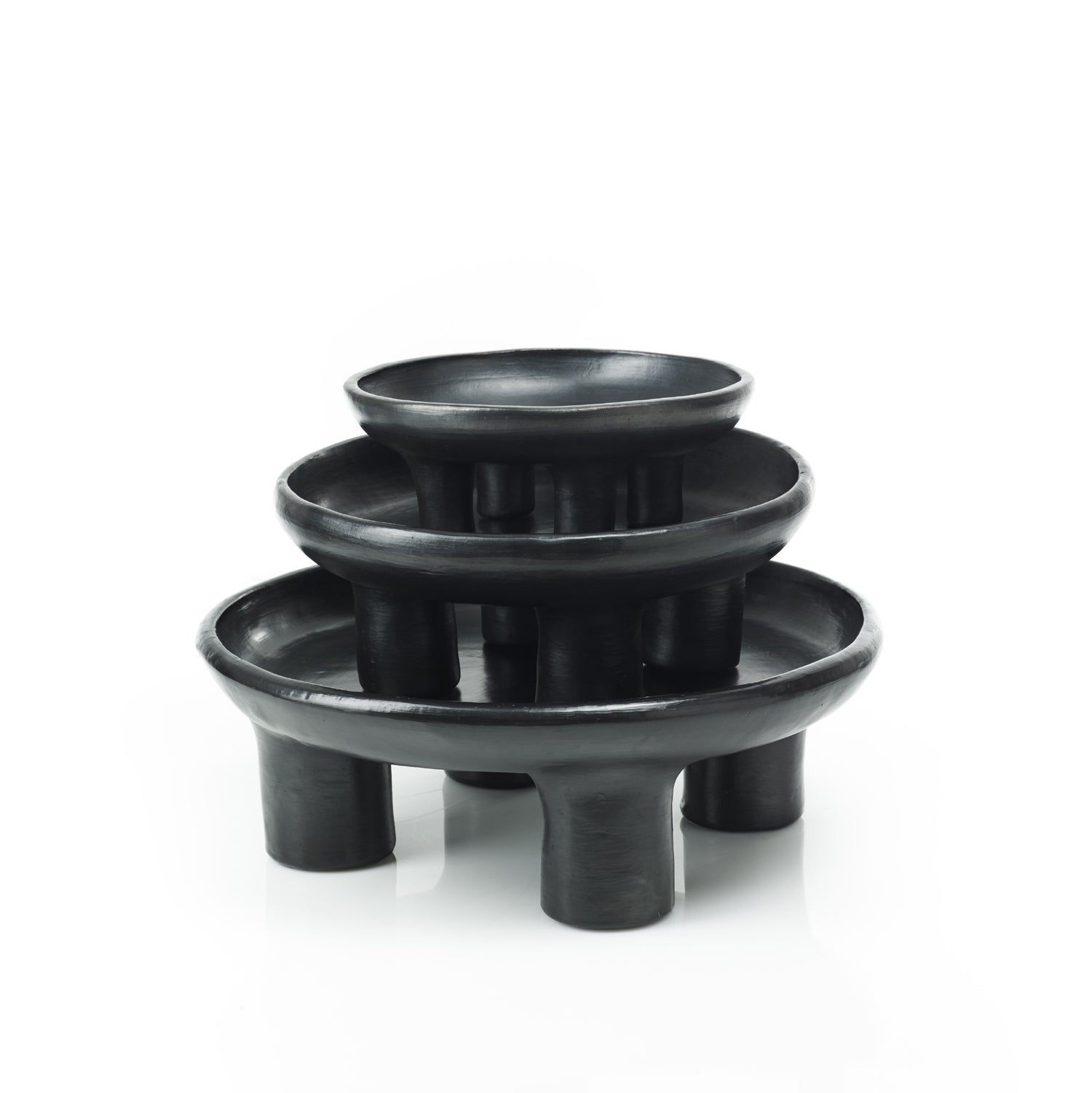 The Ames Barro Tray 1 by Ames features three black, round ceramic trays of different sizes stacked atop each other on short cylindrical legs, highlighting handmade Colombian craftsmanship against a white background.