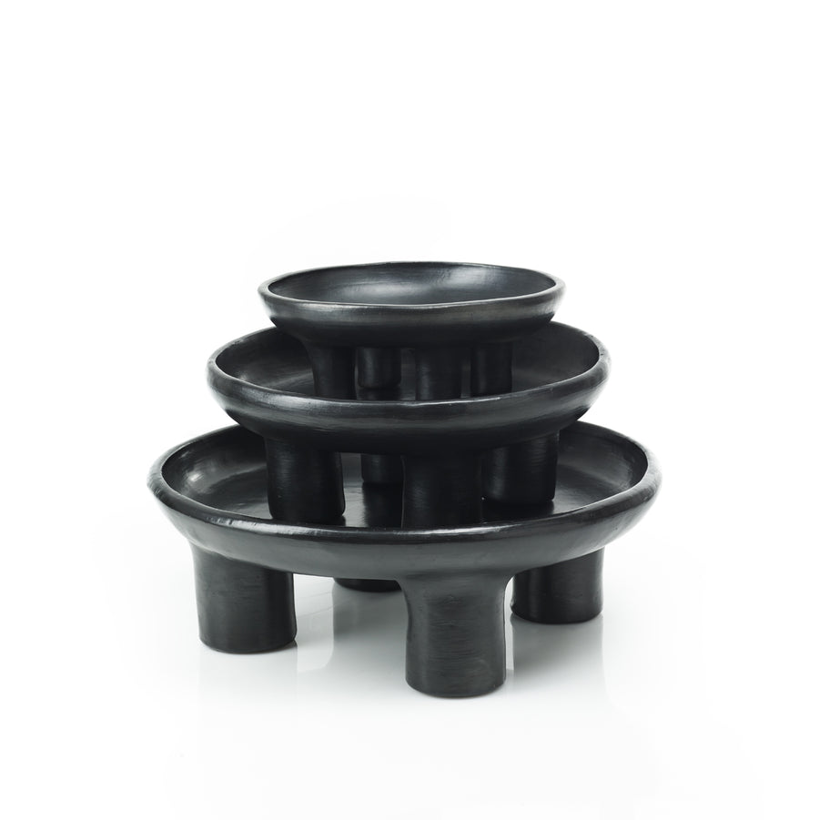 The Ames Barro Tray 1 by Ames features three black, round ceramic trays of different sizes stacked atop each other on short cylindrical legs, highlighting handmade Colombian craftsmanship against a white background.