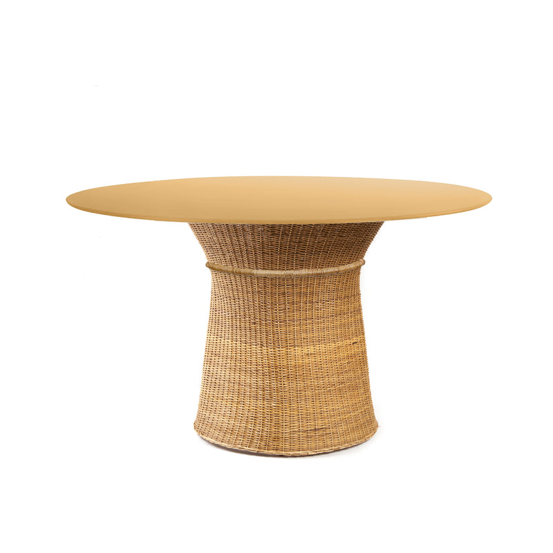 The Ames Caribe Natural Dining Table by Ames features a smooth, light brown round top and a woven wicker-style cylindrical base. Designed to complement Caribe chairs by Sebastian Herkner, it stands out against a plain white background.
