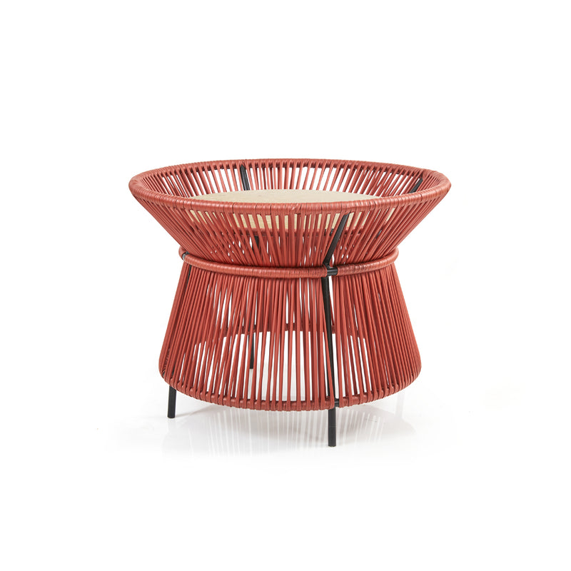 The Caribe Chic Basket Table by Ames is a modern, hourglass-shaped side table with a red woven wire frame crafted using the Momposino weaving technique and a wooden top. The tightly packed wires create a geometric pattern, making it an elegant piece in the Caribe Chic Series.