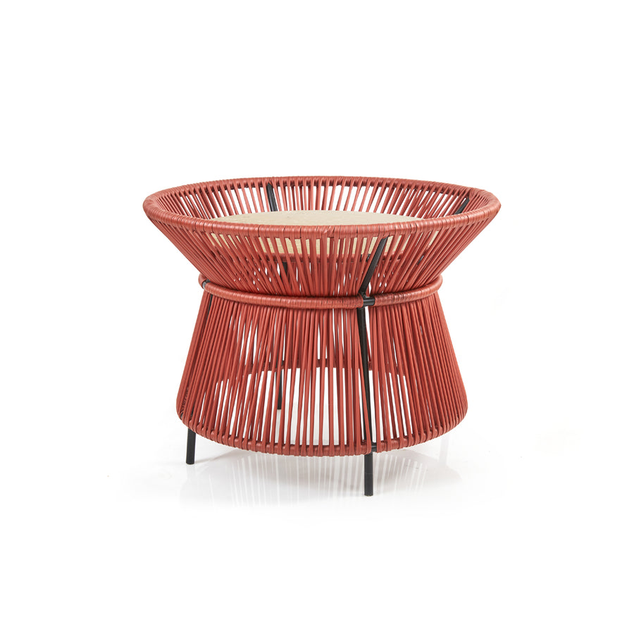 The Caribe Chic Basket Table by Ames is a modern, hourglass-shaped side table with a red woven wire frame crafted using the Momposino weaving technique and a wooden top. The tightly packed wires create a geometric pattern, making it an elegant piece in the Caribe Chic Series.