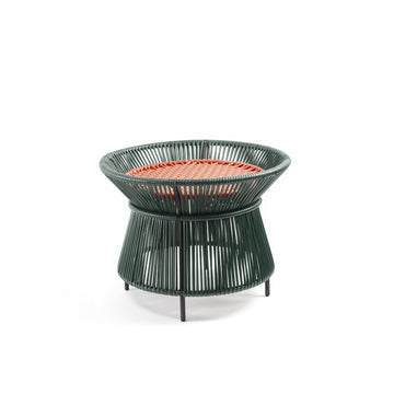 The Caribe Chic Basket Table by Ames is a small, round stool with a green wireframe structure and a red woven top made from recycled plastic cord. Its base slightly flares, standing on short black legs, combining modern minimalism with traditional Momposino weaving.