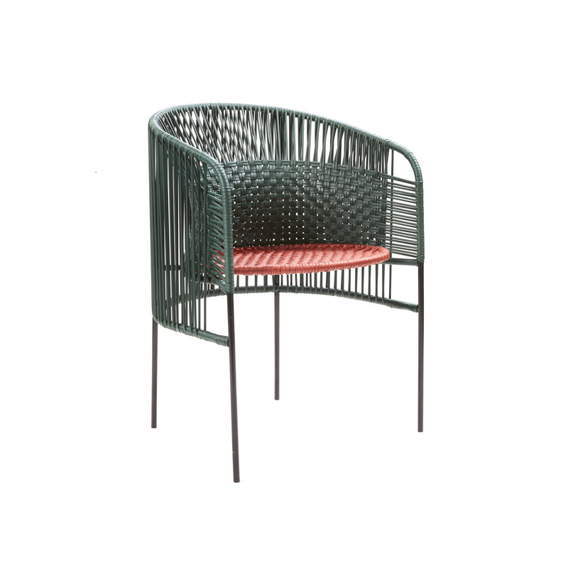 The Caribe Chic Dining Chair by Ames, designed by Sebastian Herkner, features a rounded green frame made from recycled plastic cord and an orange cushion. Its slender black legs offer a stylish mix of natural and contemporary design elements.