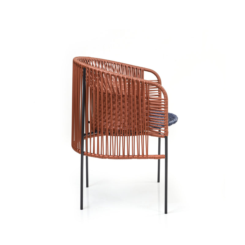 Ames Caribe Chic Dining Chair showcases Sebastian Herkners style with a modern rounded design, woven orange back and seat made from recycled plastic cord, slender black metal legs, and a blue cushion against a white backdrop.