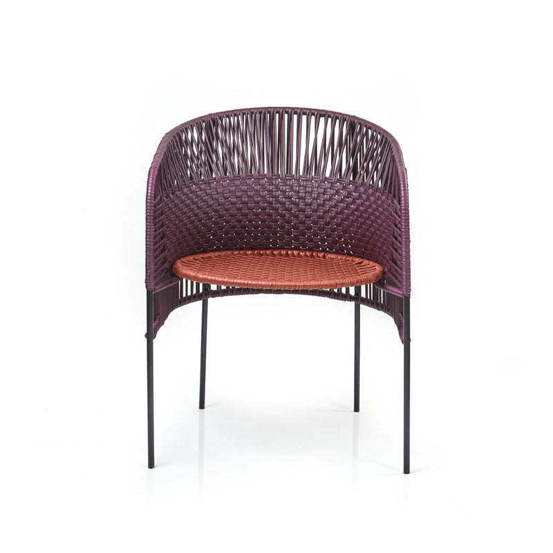 Designed by Sebastian Herkner, the Ames Caribe Chic Dining Chair features a modern design with a curved, woven back of dark purple and a bright orange seat made from recycled plastic cords. It stands on four slender black legs.