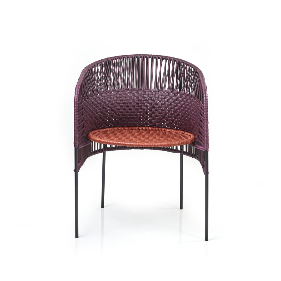 Designed by Sebastian Herkner, the Ames Caribe Chic Dining Chair features a modern design with a curved, woven back of dark purple and a bright orange seat made from recycled plastic cords. It stands on four slender black legs.
