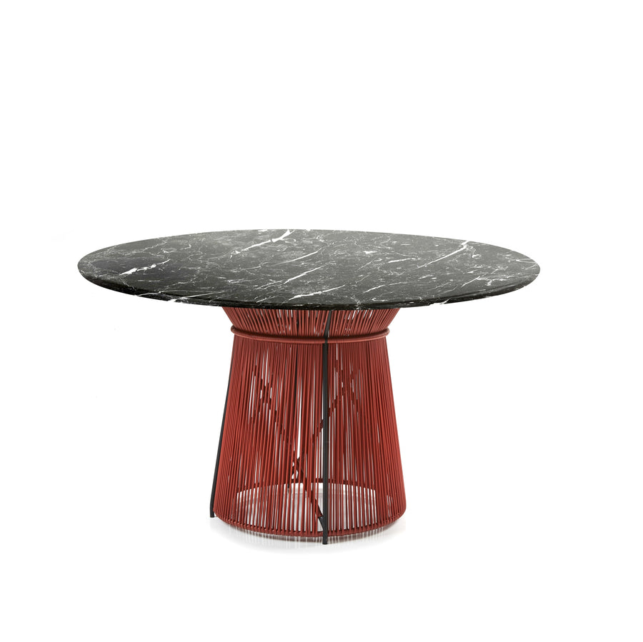 The Ames Caribe Chic Dining Table by Sebastian Herkner features a black marble round top and a red open-pattern metal base, inspired by the Caribe Chic series. Designed by Ames, it stands out against a plain white background.