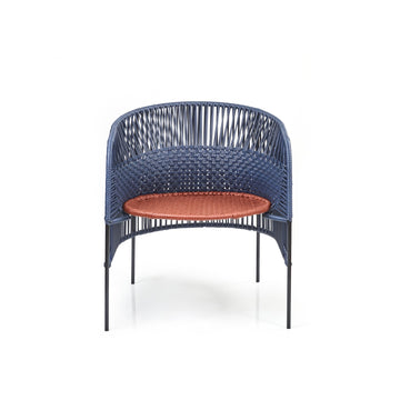 The Ames Caribe Chic Lounge Chair by Ames, designed by Sebastian Herkner, showcases a blue woven backrest and sides with Colombian craftsmanship, thin black legs, and a circular orange woven seat, all set against a white background.