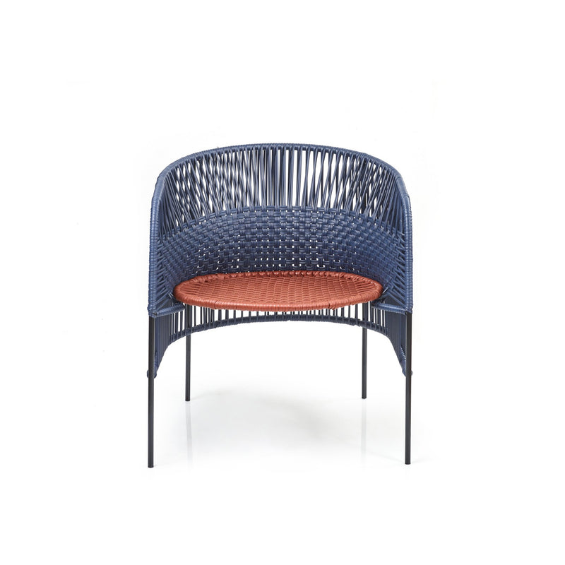 The Ames Caribe Chic Lounge Chair by Ames, designed by Sebastian Herkner, showcases a blue woven backrest and sides with Colombian craftsmanship, thin black legs, and a circular orange woven seat, all set against a white background.