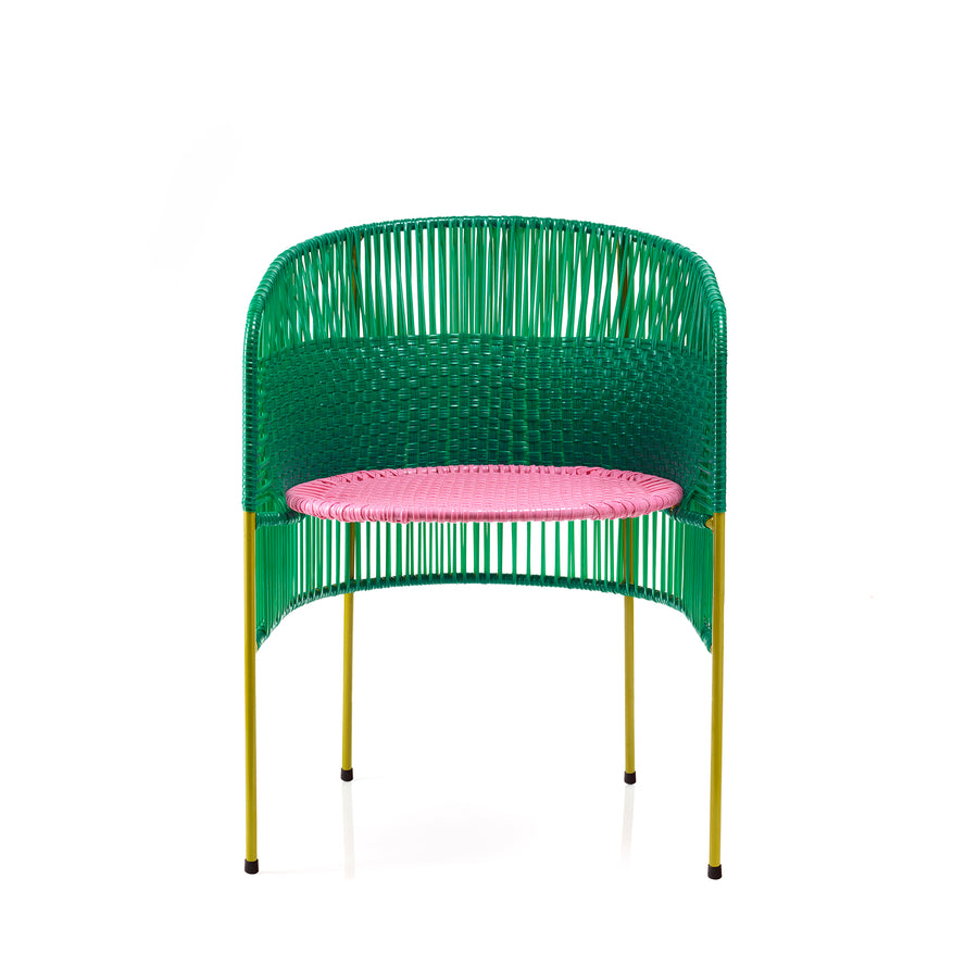 The Caribe Dining Chair by Ames features a vibrant design with a green woven backrest, pink seat, and slender yellow legs. Inspired by momposino weaving from the Caribbean coast, its open weave detail gives it a modern, airy look ideal for outdoor use.