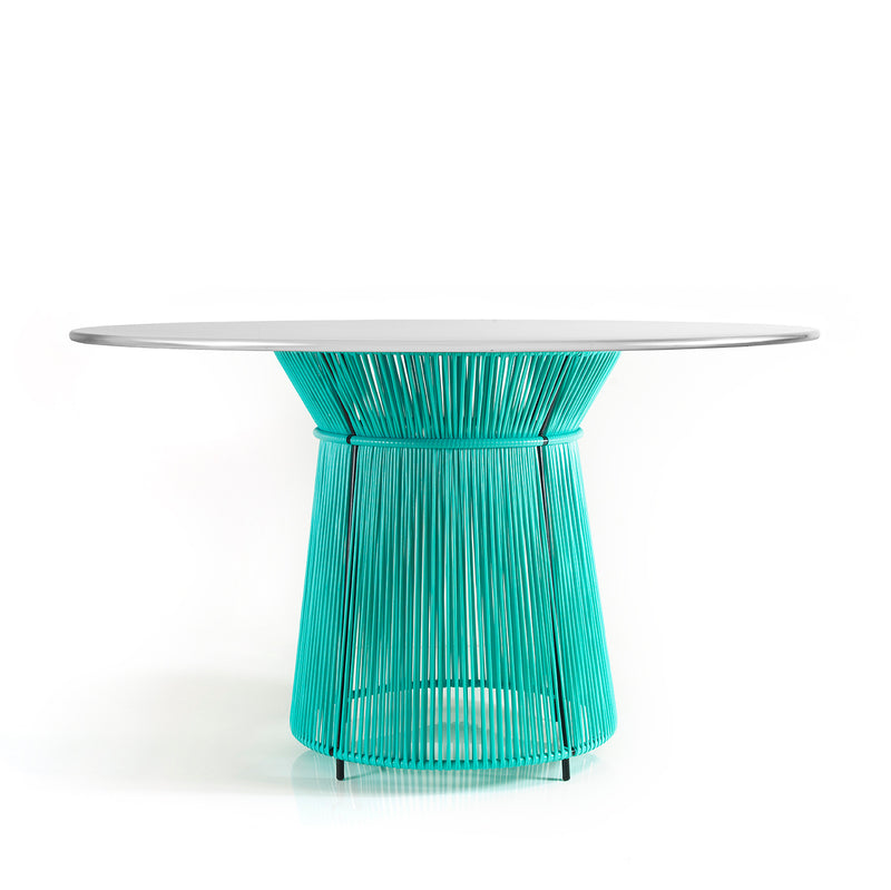 The Caribe Dining Table by Ames features a sleek white top and a vibrant turquoise base made of artistic vertical rods. Its part of our outdoor furniture collection and adds Caribbean flair against a plain white backdrop.