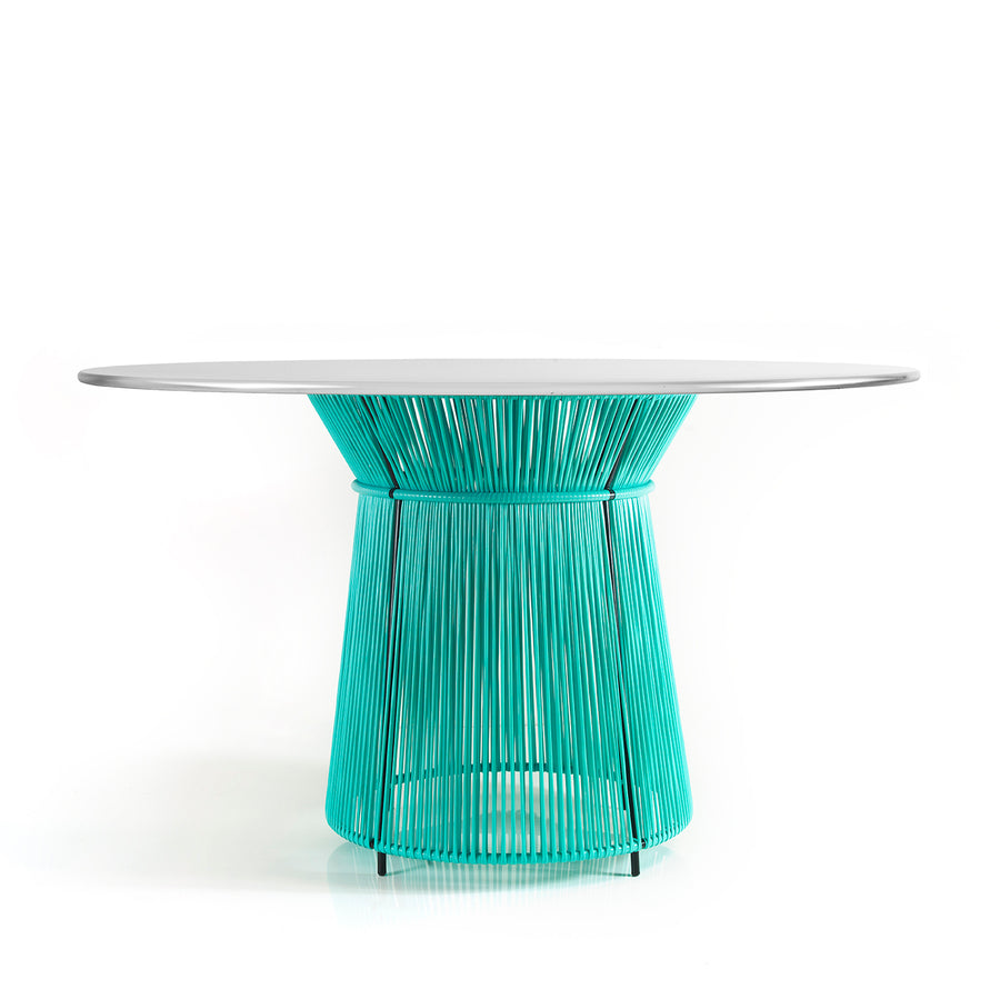 The Caribe Dining Table by Ames features a sleek white top and a vibrant turquoise base made of artistic vertical rods. Its part of our outdoor furniture collection and adds Caribbean flair against a plain white backdrop.