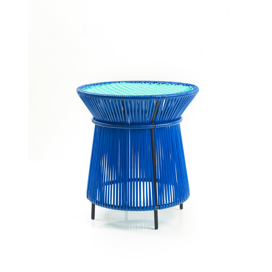 The Ames Caribe High Table by Ames, designed by Sebastian Herkner, features a round top with bright blue woven strings and slim black metal legs—a striking, modern choice for vibrant outdoor settings.