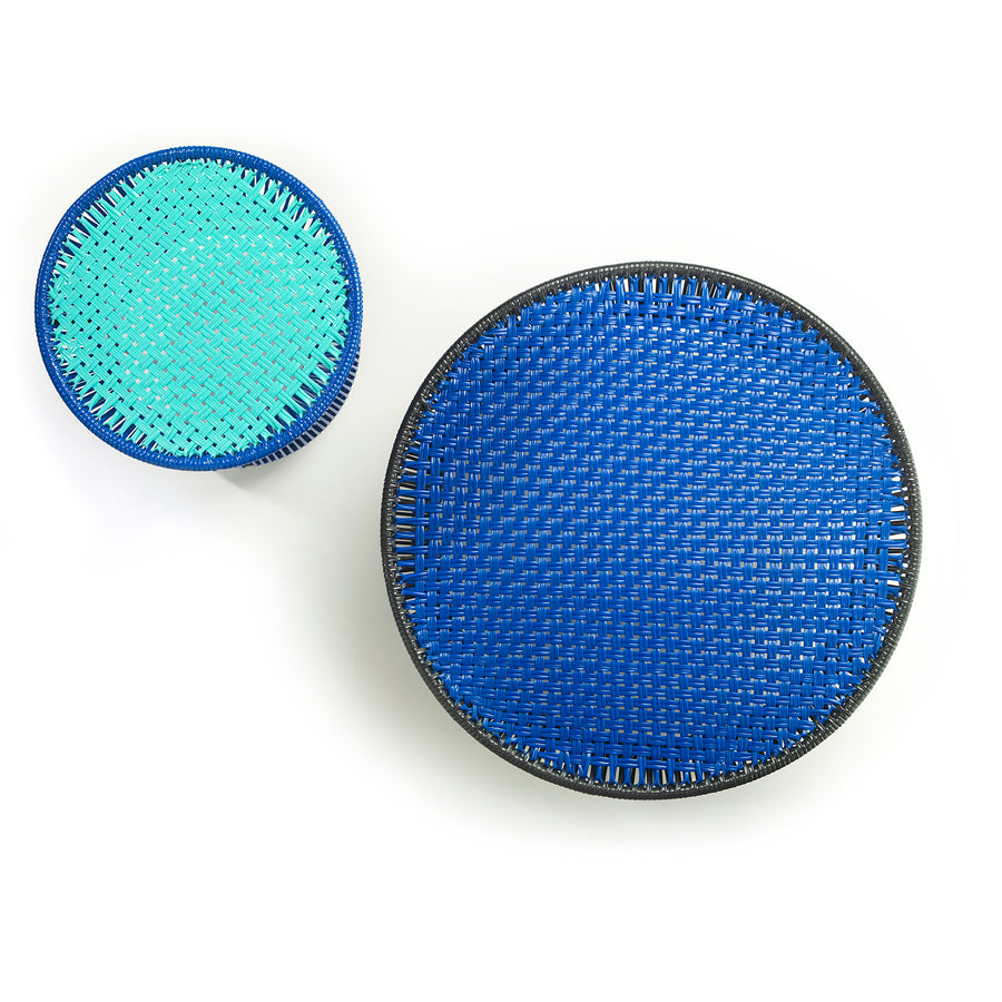 Two Ames Caribe Low Tables by Ames, designed by Sebastian Herkner, feature woven surfaces: the larger is dark blue with a black rim, the smaller is turquoise and blue. Both outdoor tables are shown from above on a white background.