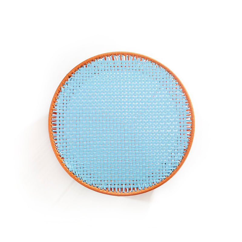 The Ames Caribe Low Table by Ames, designed by Sebastian Herkner, boasts a round woven design with a light blue center and brown rim—an ideal accent for outdoor furniture, shown from above against a white background.