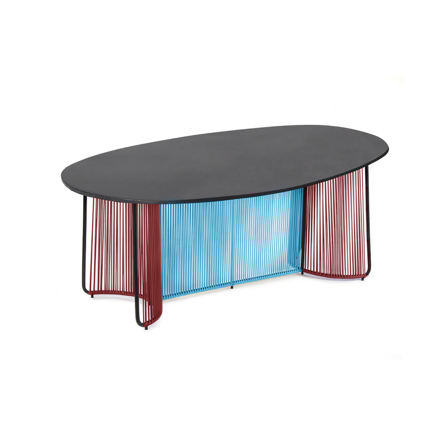The Ames Cartagenas Dining Table by Ames, designed by Sebastian Herkner, features an oval black marble top and slim vertical metal rods in alternating blue and red hues, set against a white background.