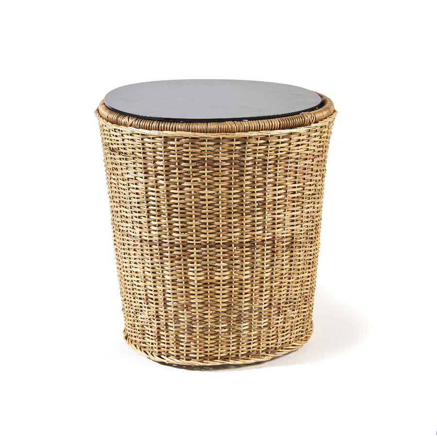 The Ames Cartagenas Natural Sidetable, featuring a round wicker design with a woven rattan build and a flat, dark lid, captures the aesthetic of Sebastian Herkners furniture series. Set against a white background, it showcases elegance and impeccable craftsmanship.