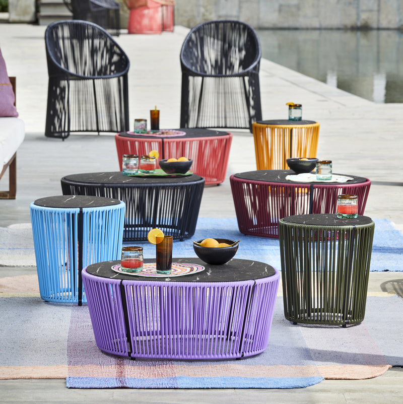 Brightening the poolside, Ames outdoor furniture features woven designs and the Ames Cartagenas Coffee Table, with vibrant chairs and tables on patterned rugs set for guests with drinks and snacks.