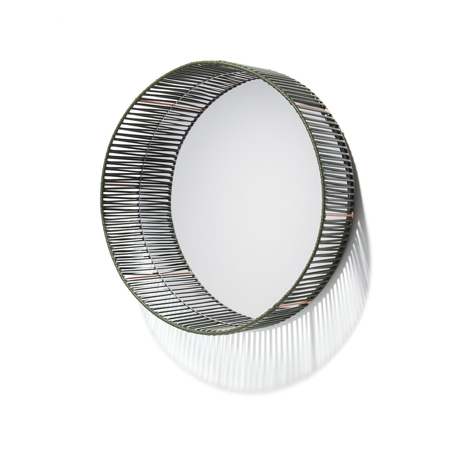 The Cesta Mirror by Ames features a circular design with a decorative black wire frame that projects outward, casting intricate shadow patterns. Its minimalist style and recycled PVC lace enhance modern aesthetics, making it ideal for spaces seeking eco-friendly elegance.