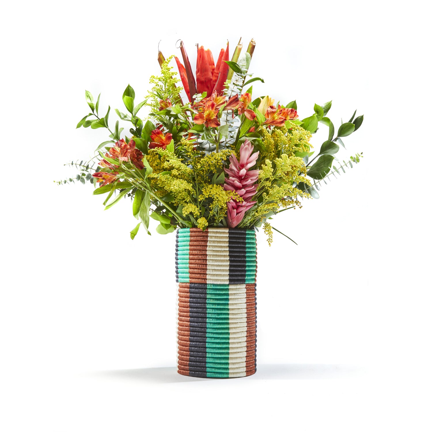 A vibrant floral arrangement with red, pink, and yellow flowers and green foliage in a colorful Choco Vase by Ames. It features a pattern of horizontal and vertical stripes in blue, brown, green, and white.