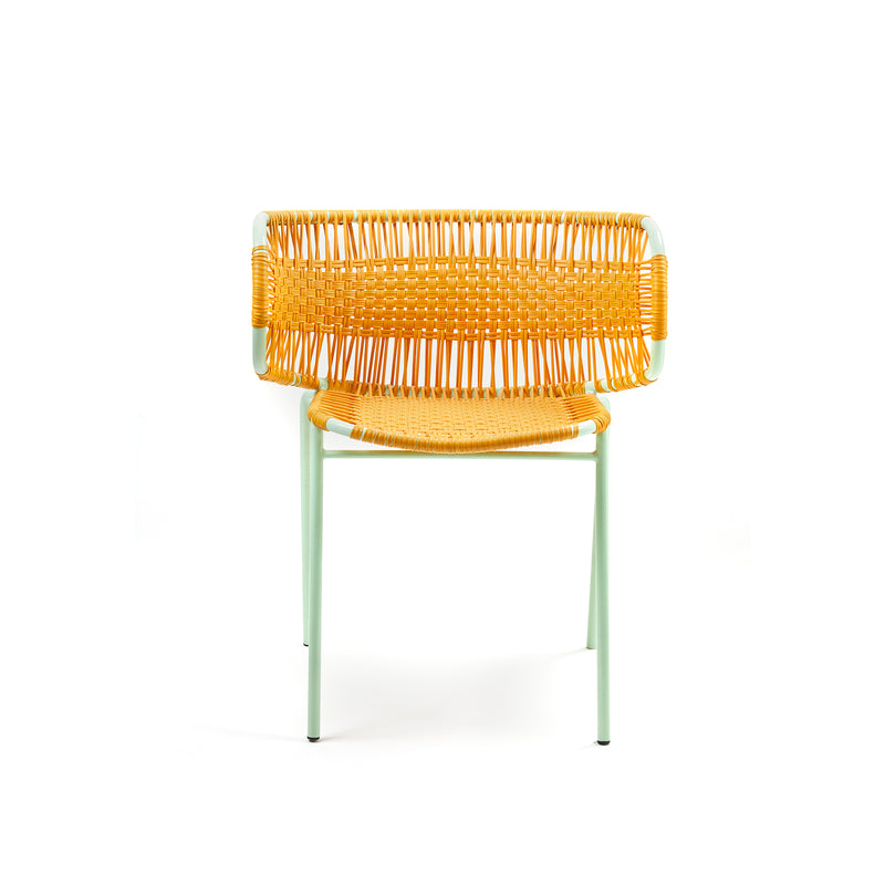 Ames Cielo Armchair has a modern aesthetic with a yellow woven seat and back, crafted using traditional weaving. Its supported by a light green metal frame with four slender legs, emphasizing minimalist geometric shapes against a white backdrop.