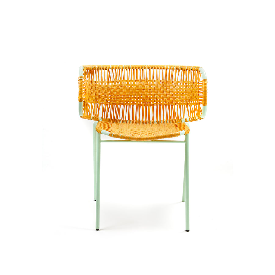 Ames Cielo Armchair has a modern aesthetic with a yellow woven seat and back, crafted using traditional weaving. Its supported by a light green metal frame with four slender legs, emphasizing minimalist geometric shapes against a white backdrop.