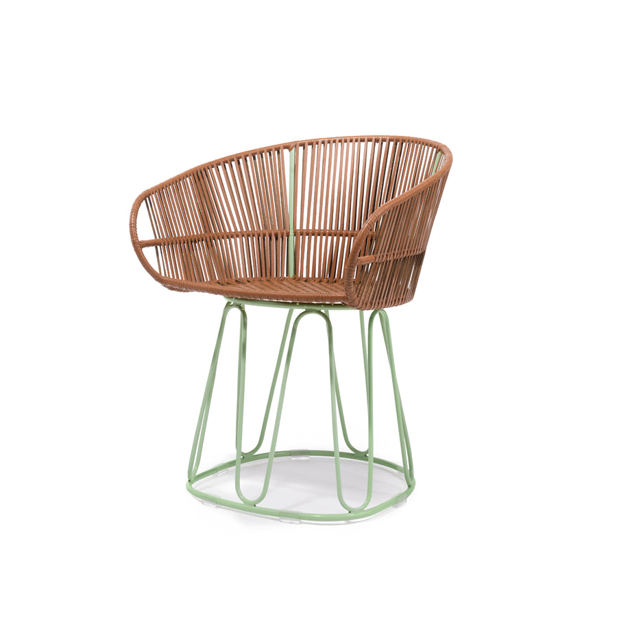 As part of Ames CIRCO collection, the Circo Leather Dining Chair boasts a light green metal base and a brown woven rattan seat. Its rounded open-back design seamlessly merges modern and natural elements, reflecting Sebastian Herkners artistry.