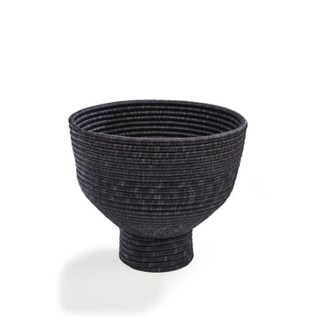 The Ames La Che Pot by Ames is a black, textured bowl with a wide rim and narrow base, inspired by Colombian culture. Horizontal ridges encircle its surface and it stands out against a plain white background.