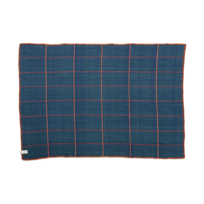 The Ames Manta Plaid by Ames features a blue rectangular design with an orange and white grid, orange-edged stitching, and a small fabric tag—highlighting traditional Colombian craftsmanship and displayed flat on a white background.