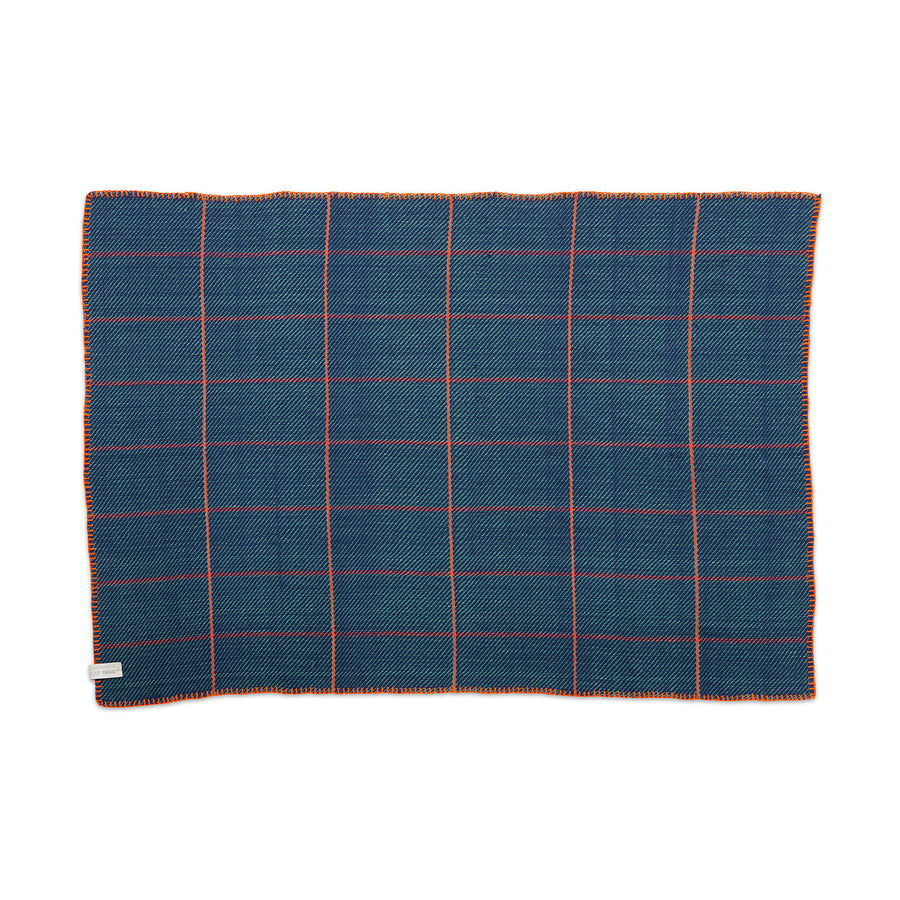 The Ames Manta Plaid by Ames features a blue rectangular design with an orange and white grid, orange-edged stitching, and a small fabric tag—highlighting traditional Colombian craftsmanship and displayed flat on a white background.
