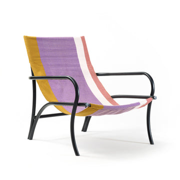 The Maraca Lounge Chair by Ames features a black metal frame and a vibrant fabric seat, reminiscent of Colombian hammocks, with stripes of purple, mustard yellow, white, and pink. Its seamless curved backrest and seat are set against a plain white background.