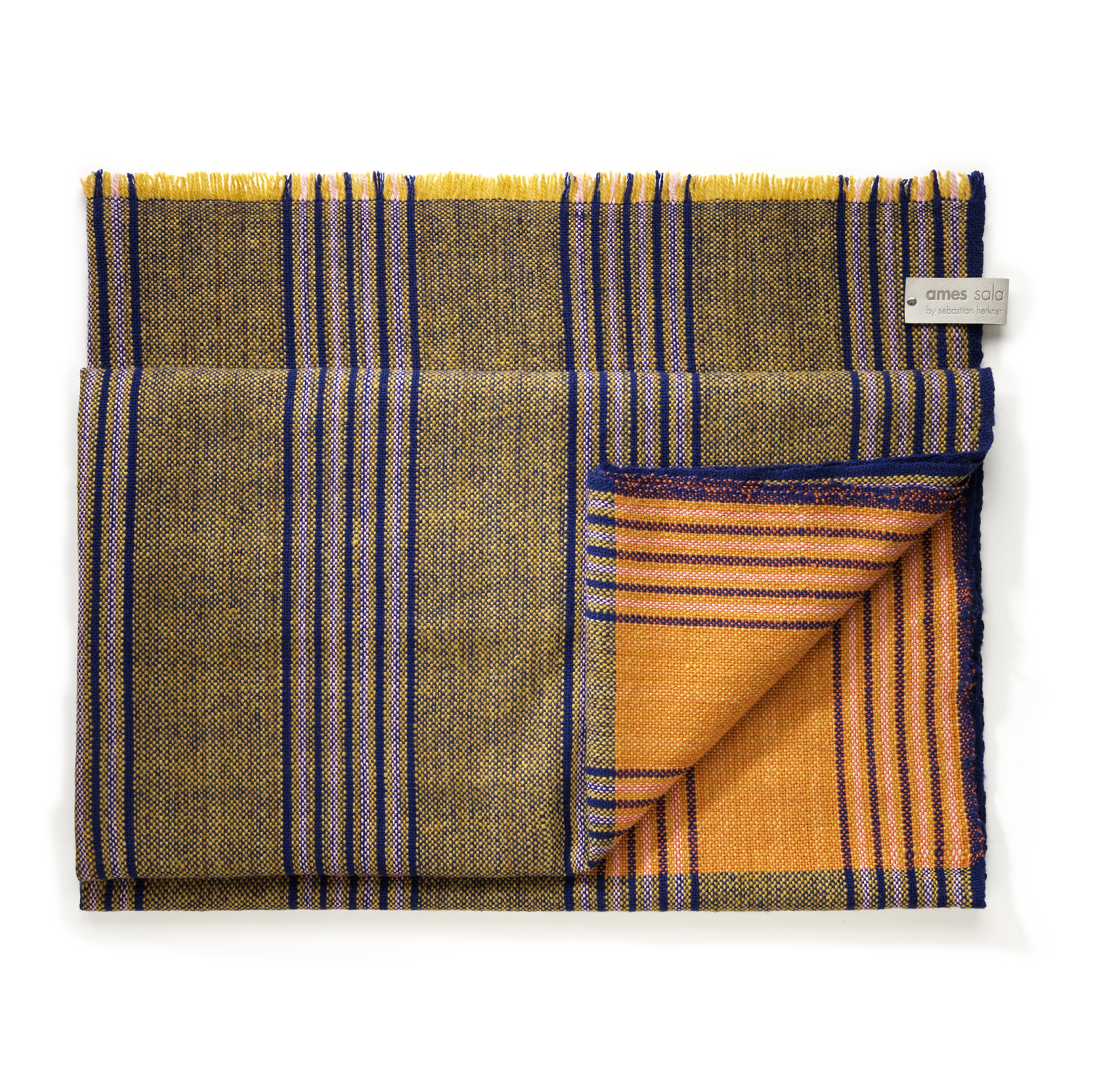 The Ames Mulera Throw by Ames features a plaid pattern in yellow, olive, blue, and beige with an orange and blue striped underside and an “ames sala” label—ideal for those wanting a cozy yet lightweight throw.