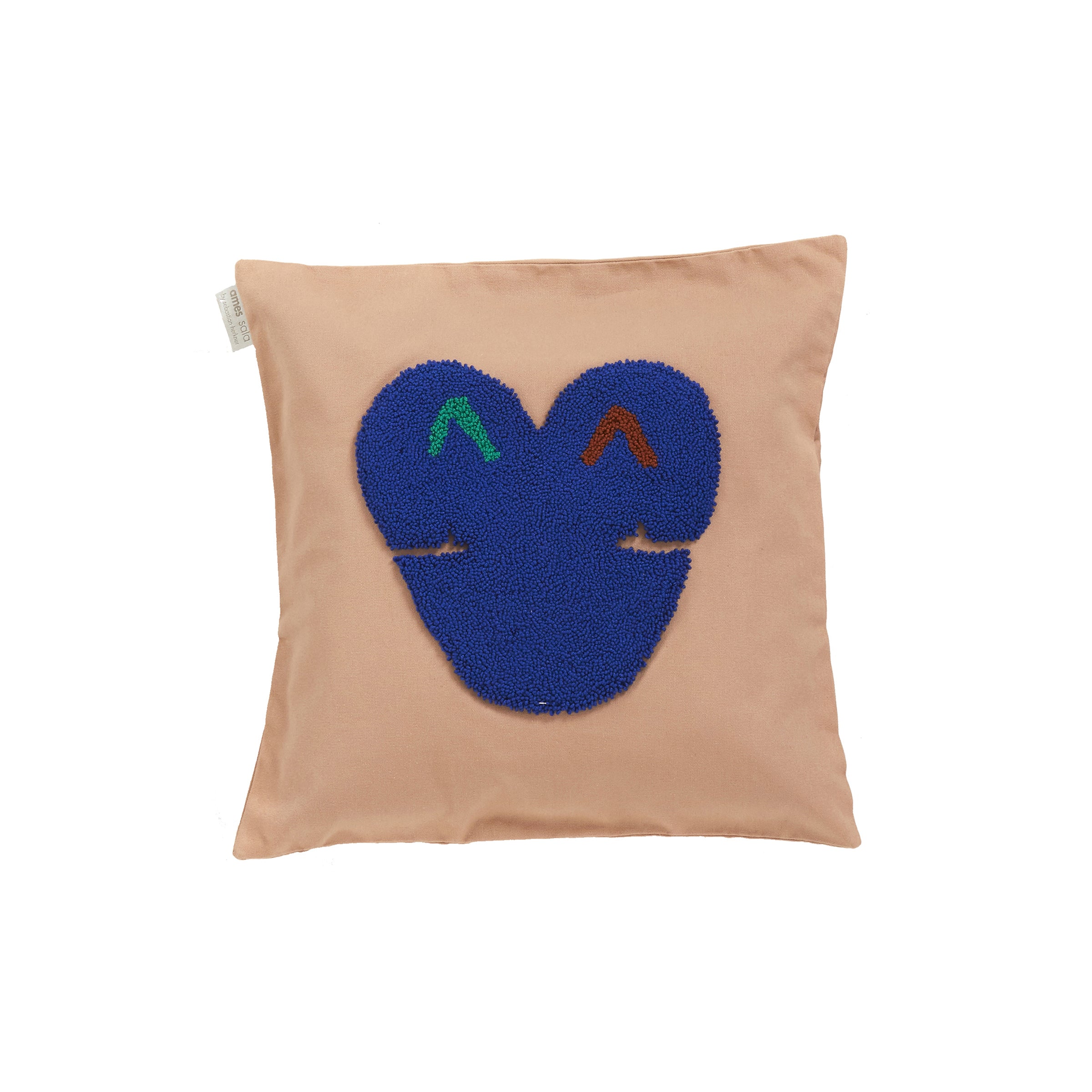 The Ames Nido Kukuy collection includes a beige square cushion with a textured blue face design, accented with green and red for eyes on a white background. Made from 100% cotton, it features a whimsical expression and has a small side label.
