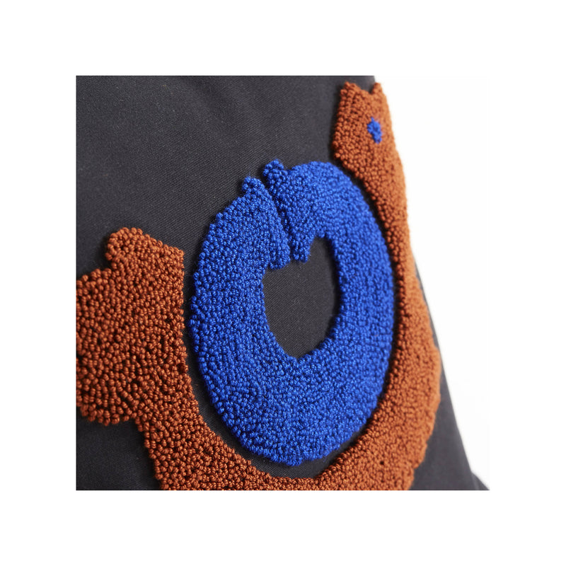 A close-up of the Ames Nido Pichu fabric patch by Ames, showcasing a blue circle and brown curved shapes with a beaded texture on a black background, inspired by Sebastian Herkner’s Nido cushions.