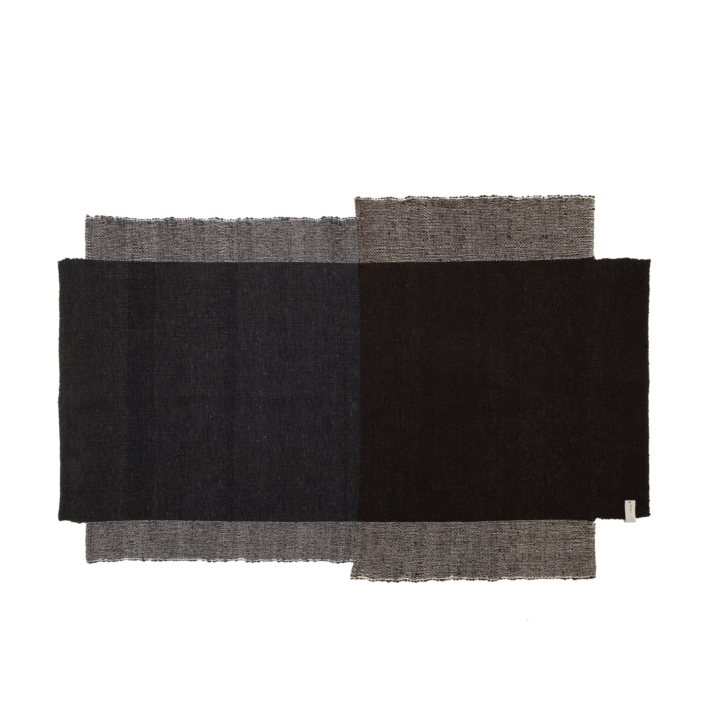 The Nobsa Rug by Ames is a hand-woven, rectangular wool textile. It features an abstract design with overlapping dark gray, black, and light brown sections, creating a textured look with frayed edges that reflect the artisanal heritage of Colombias city of Nobsa.