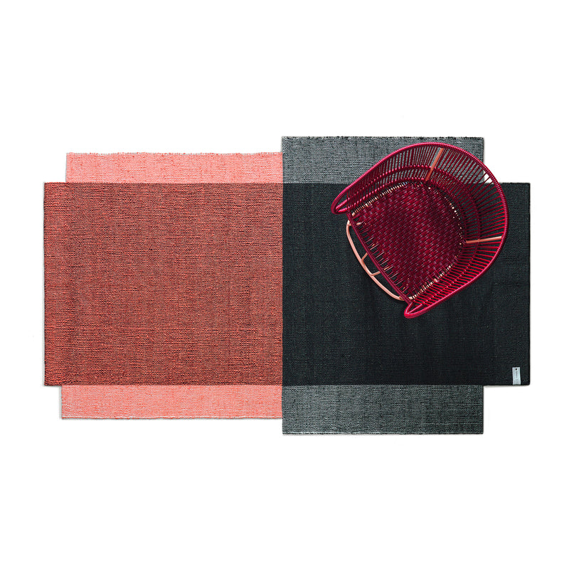 A top view shows two overlapping rectangular rugs, one red and one black. A hand-woven wool Nobsa Rug by Ames from Nobsa is showcased, complemented by a red woven chair with a wave pattern on the black rug, crafting a modern geometric look.