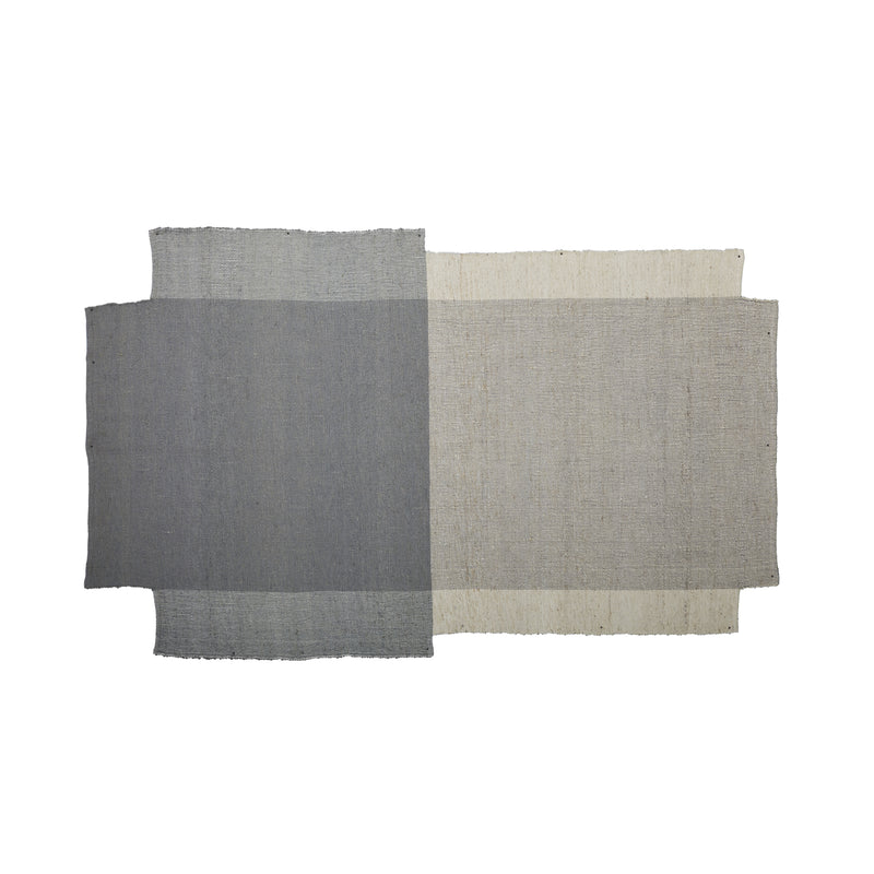 The Nobsa Rug by Ames features a rectangular design with hand-woven wool panels in dark gray and light beige. These intersecting panels evoke the craftsmanship of Nobsa rugs from the Colombian city, offering a subtle contrast in shades and texture.