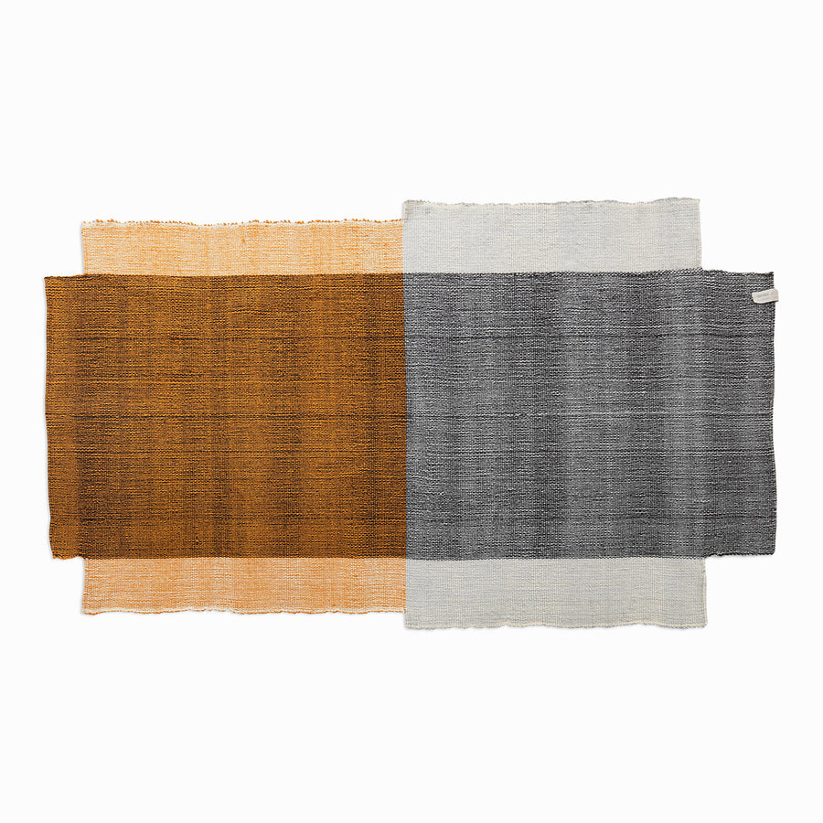This rectangular fabric swatch has a brown and orange gradient section and a gray with light blue section, reminiscent of Nobsa rugs by Ames. The textured woven appearance mimics the artisanal charm of hand-woven wool traditions from Nobsa, Colombia.