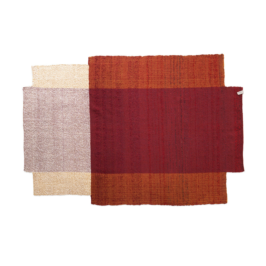 Three overlapping rectangular rugs in red, brown, and cream are arranged horizontally. The red and brown Nobsa Rugs by Ames feature a hand-woven wool texture typical of Nobsa craftsmanship, while the cream rug offers a soft feel also reflecting Colombian artistry.
