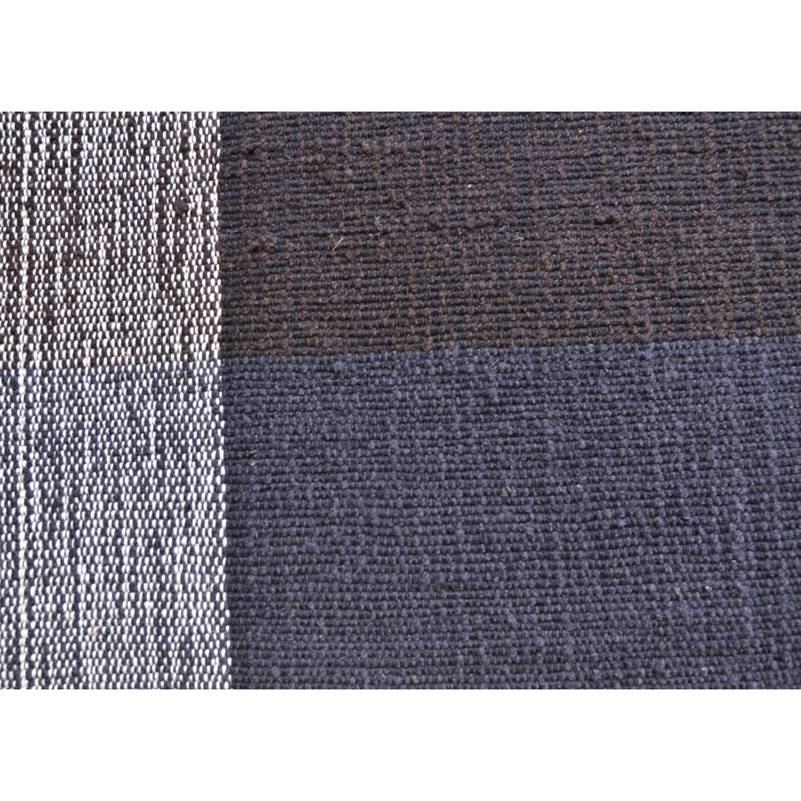 Ames Nobsa Rug features a pattern of alternating stripes: the left showcases thin, tightly woven black and white stripes reminiscent of hand-woven wool from Colombian Nobsa, while the right has wider black sections with a textured look.