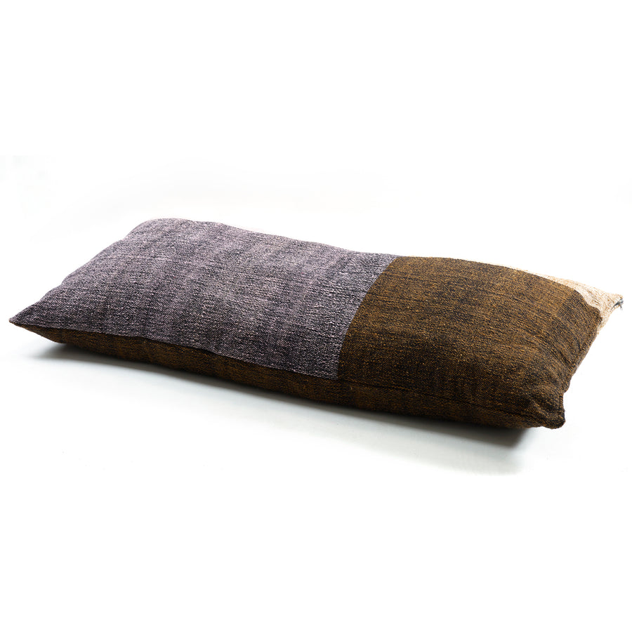 The Ames Nobsa Cushion by Ames is a rectangular pillow made of hand-woven wool with a textured cover, featuring two color blocks: muted purple on one side and warm brown on the other, inspired by traditional Nobsa pillows.