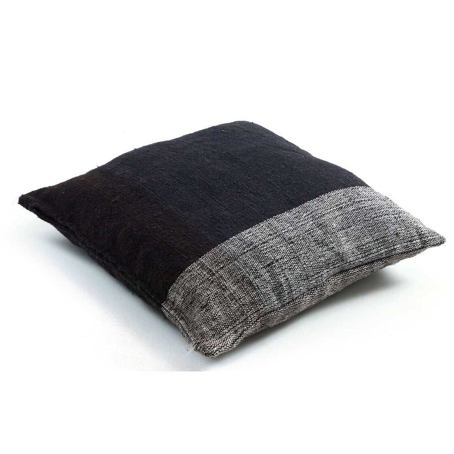 The Ames Nobsa Cushion by Ames is a square, hand-woven wool pillow in textured dark brown with a wide light gray band along one edge, shown on a white background.