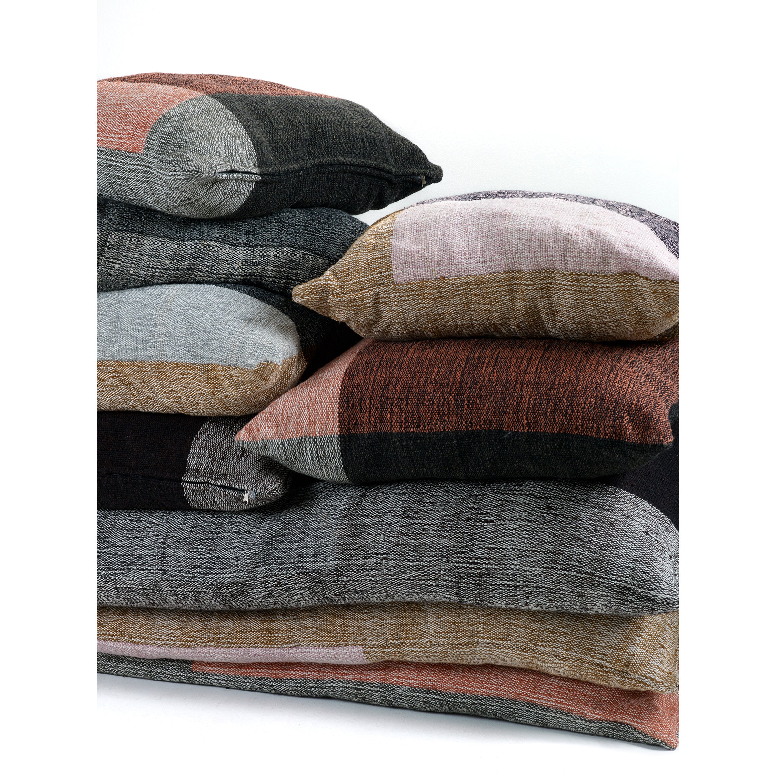 A stack of five Ames Nobsa Cushions by Ames, crafted from hand-woven wool in gray, black, brown, and muted pink, are arranged against a plain white background.