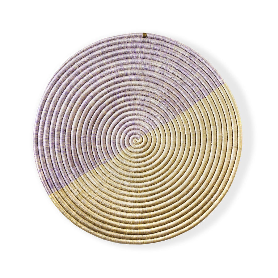 The Ames Ojitos Wall Decoration Andes by Ames is a round, woven basket wall decor crafted from fique palm fibers with a spiral pattern. Half is light tan, the other half muted lavender, offering subtle geometric contrast for any space.