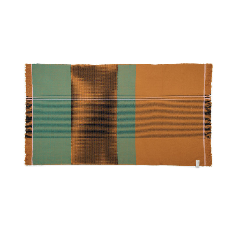 The Ames Ruana Throw features a rectangular design with vertical and horizontal stripes in teal, mustard, and black. It highlights traditional craft techniques with contrasting color blocks and fringed side edges.