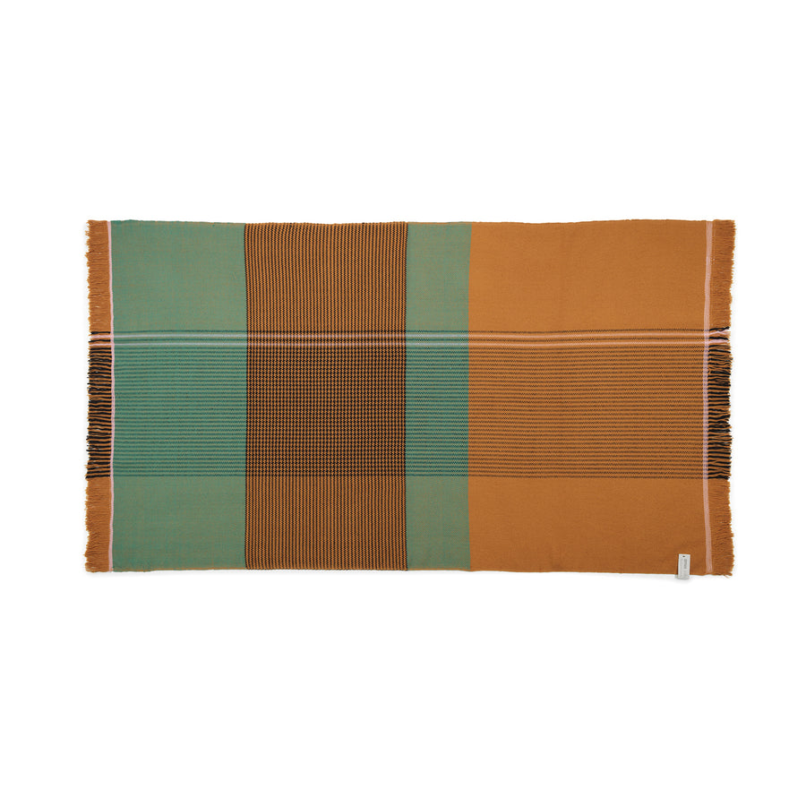 The Ames Ruana Throw features a rectangular design with vertical and horizontal stripes in teal, mustard, and black. It highlights traditional craft techniques with contrasting color blocks and fringed side edges.