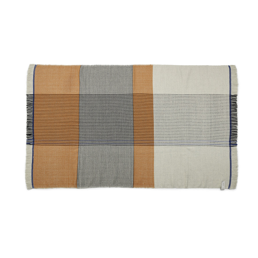 The Ames Ruana Throw is a rectangular woven blanket that uses traditional techniques and earthy tones. It features vertical and horizontal stripes in beige, brown, black, cream patterns, fringed edges like Ruana throws, and a small fabric tag on one side.